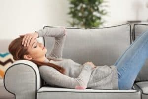 Femme allongée avec une migraine, se tenant la tête.