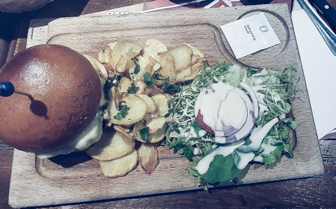 Burger avec frites et salade sur planche en bois.