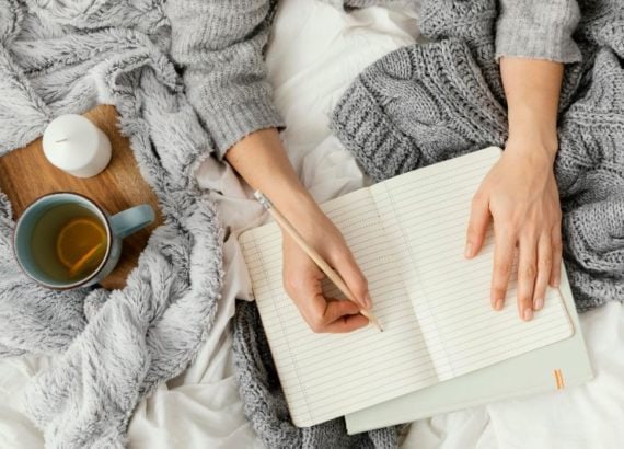 Personne écrit dans un journal avec thé et bougie.