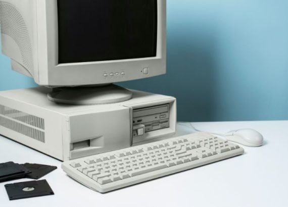 Ordinateur rétro des années 90 avec écran cathodique, clavier, souris et disquettes sur un bureau blanc.