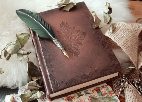 Carnet en cuir avec une plume verte et des feuilles séchées autour