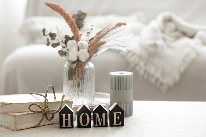 Détail d’un intérieur chaleureux avec livres, fleurs séchées et décoration “HOME”, symbole d’intimité et de recentrage personnel.