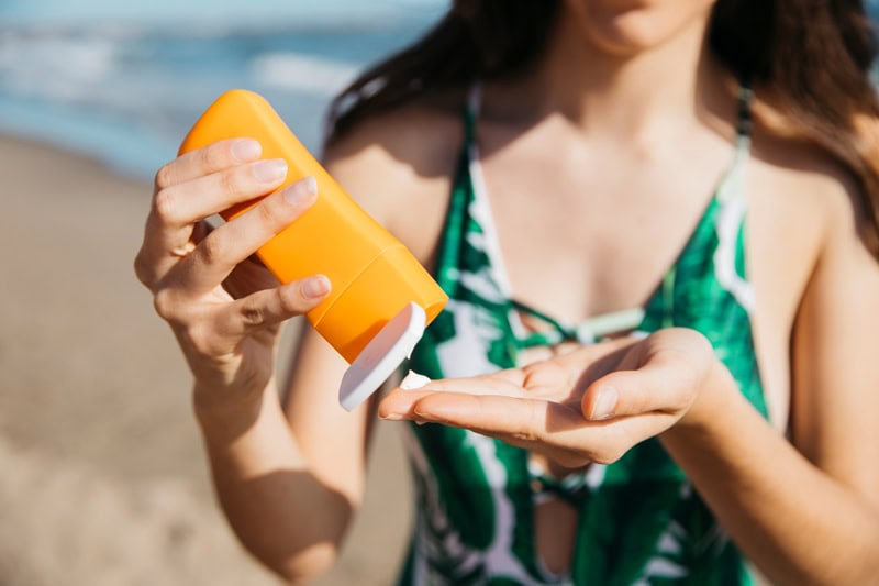 Femme appliquant de la crème solaire sur la plage pour se protéger du soleil.