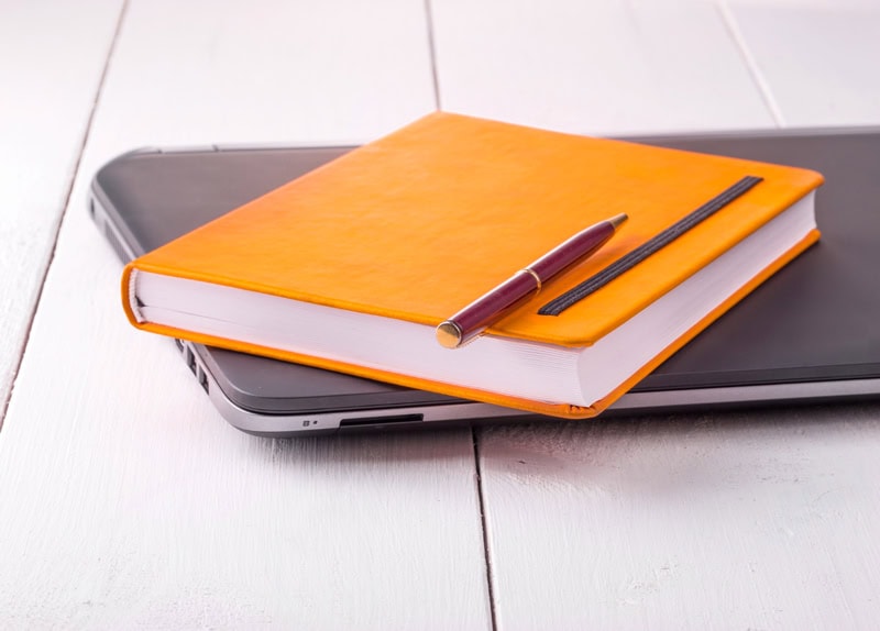 Carnet orange et stylo posés sur un ordinateur portable, représentant l’organisation et les projets du blog pour 2020.