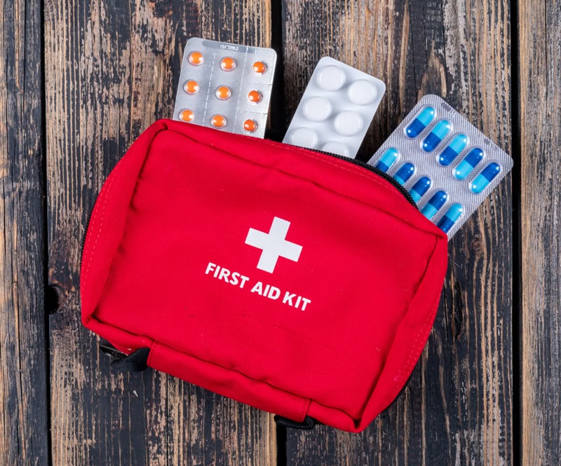 Trousse de secours rouge avec plaquettes de médicaments, posée sur une table en bois.