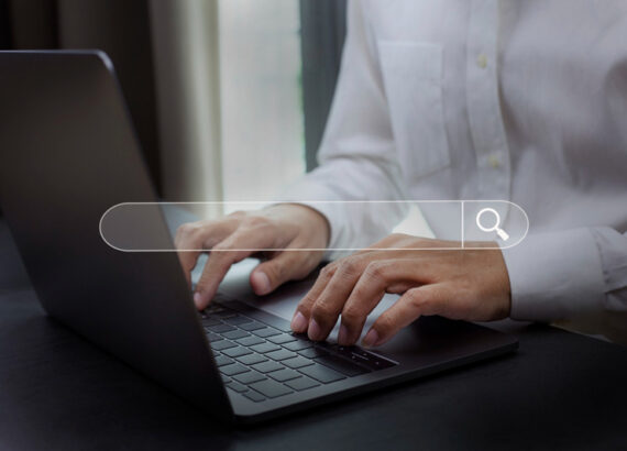 Personne tapant sur le clavier d’un ordinateur portable avec une barre de recherche virtuelle en surimpression, pour illustrer les recherches Google de l’année 2025.