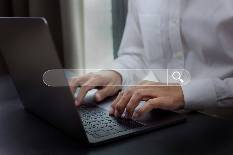 Personne tapant sur le clavier d’un ordinateur portable avec une barre de recherche virtuelle en surimpression, pour illustrer les recherches Google de l’année 2025.