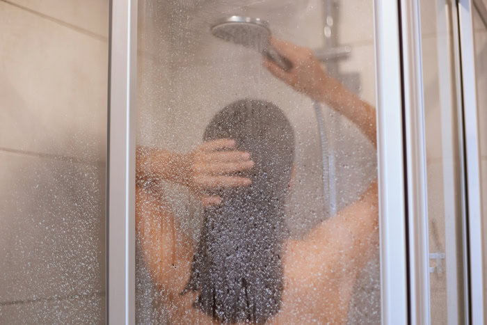 Personne sous la douche le soir derrière une paroi en verre dépoli