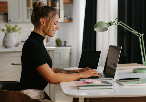 Femme souriante qui tape sur son laptop à son bureau à la maison