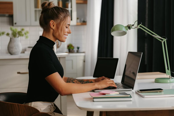 Femme souriante qui tape sur son laptop à son bureau à la maison