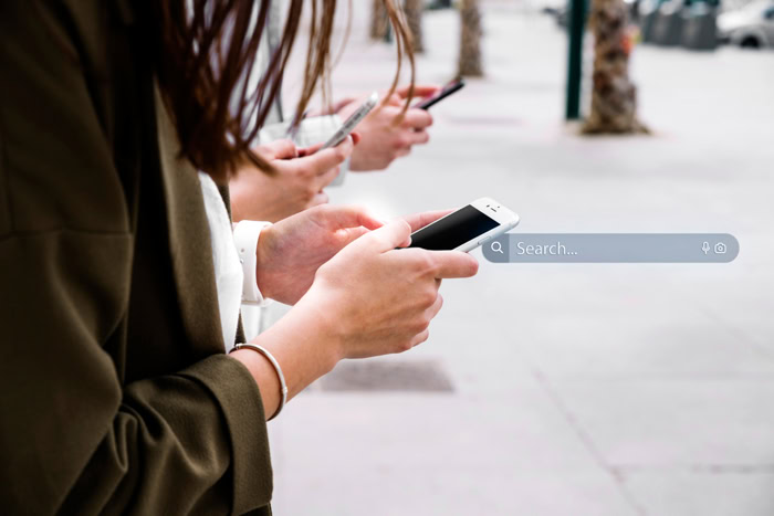 Personnes utilisant leurs smartphones avec une barre de recherche illustrant les tendances Google en 2023.