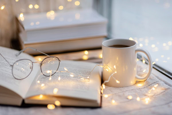 Livre ouvert avec une tasse et des lumières dans une ambiance cosy